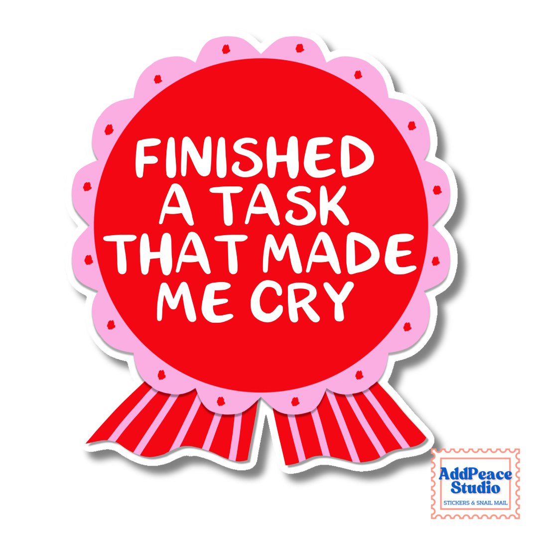 A die-cut sticker shaped like a pink and red ribbon award badge with the text 'FINISHED A TASK THAT MADE ME CRY' in white lettering, shown on a white background with a small AddPeace Studio logo in the bottom right corner.