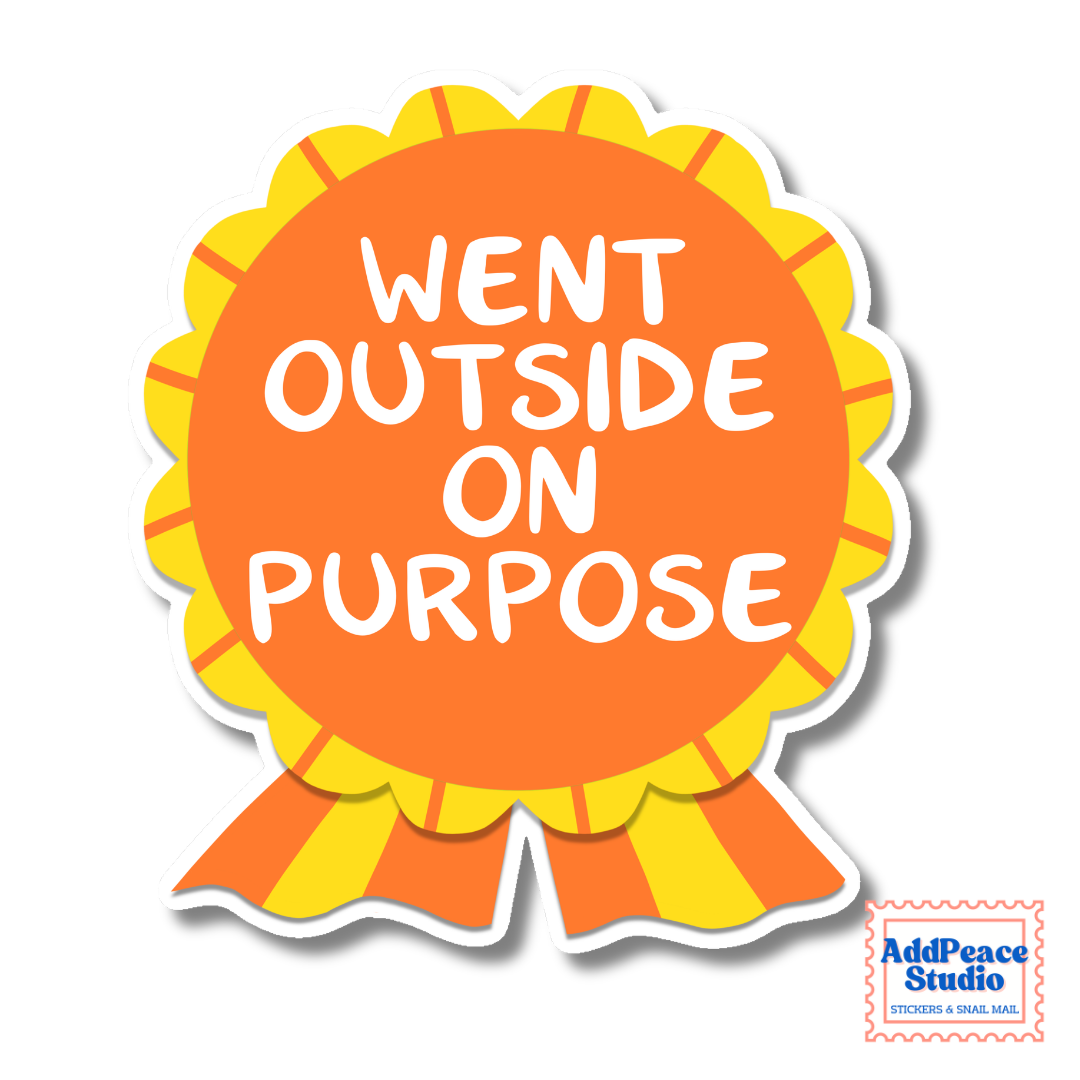 A die-cut sticker shaped like a ribbon award badge, with an orange center, yellow scalloped border, and orange and yellow striped ribbon tails. White text on the sticker reads “WENT OUTSIDE ON PURPOSE.