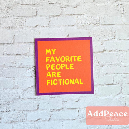 Orange sticker with yellow text 'My favorite people are fictional' on a white brick wall, featuring the brand 'AddPeace'.