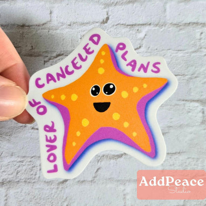 Star-shaped sticker with a smiley face and text 'CANCELED PLANS YOU LOVER' held by a hand against a light gray background.