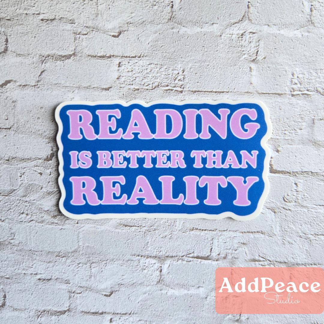 Sticker with 'READING IS BETTER THAN REALITY' text on a white brick wall, branded with AddPeace Studio.