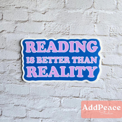 Sticker with 'READING IS BETTER THAN REALITY' text on a white brick wall, branded with AddPeace Studio.