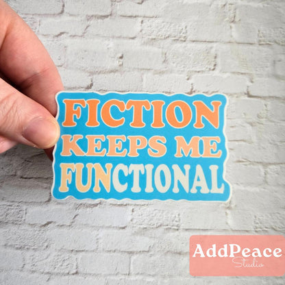 Hand holding a sticker with 'FICTION KEEPS ME FUNCTIONAL' text against a white brick wall background.