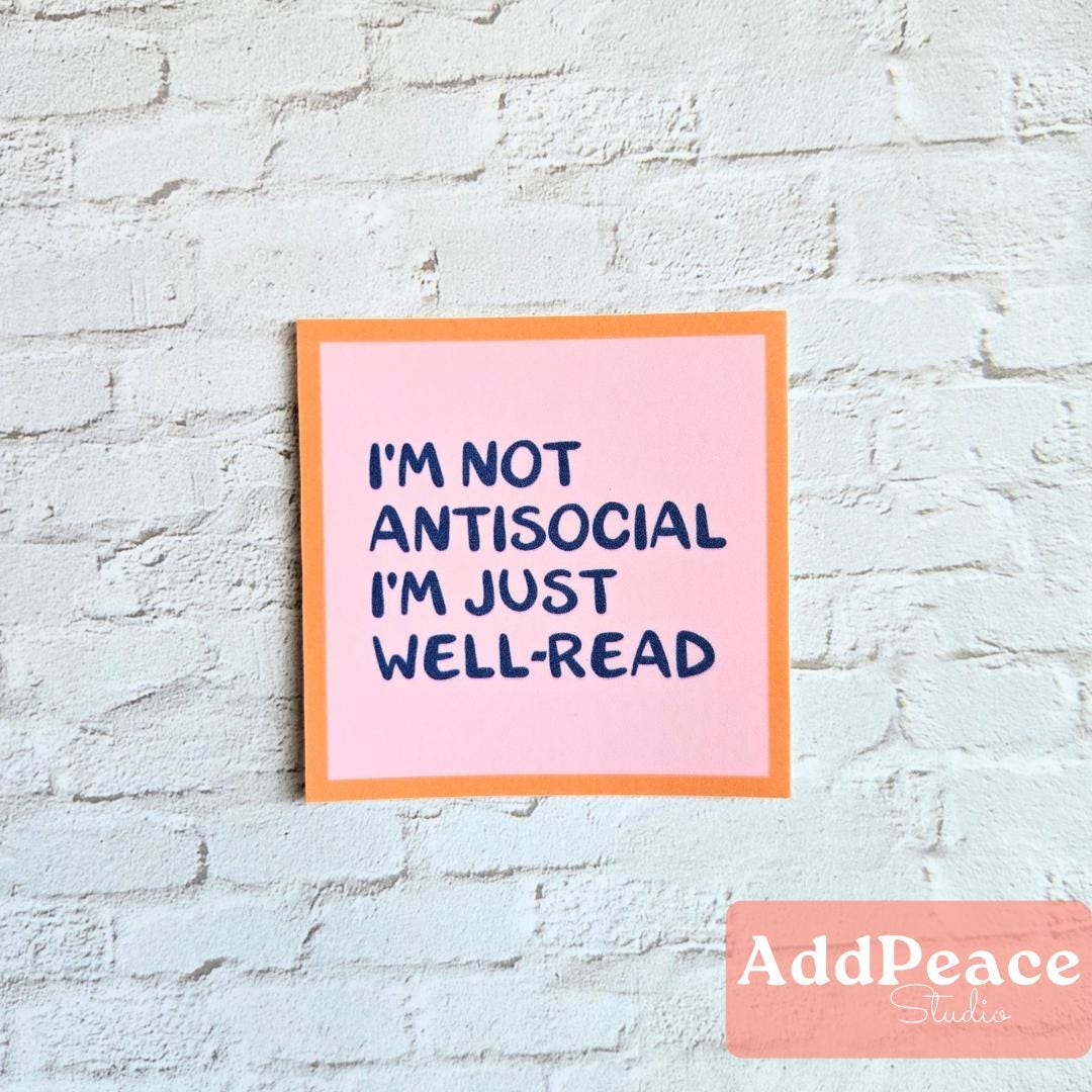 Pink sticker with text 'I'm not antisocial, I'm just well-read' on a light blue brick wall, with 'AddPeace Studio' branding.