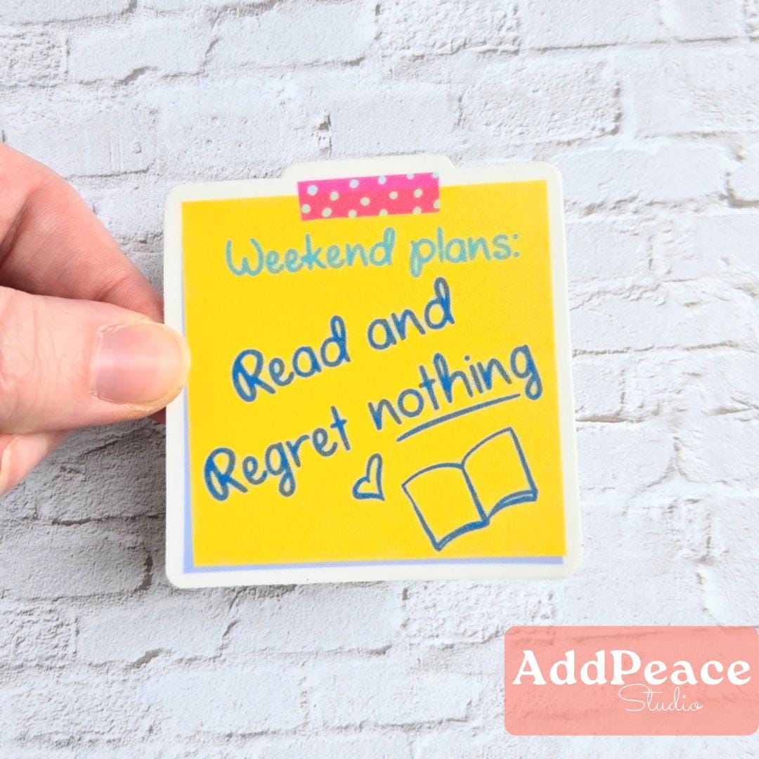 Hand holding a yellow sticker with text 'Weekend plans: Read and Regret nothing' on a white brick wall background.