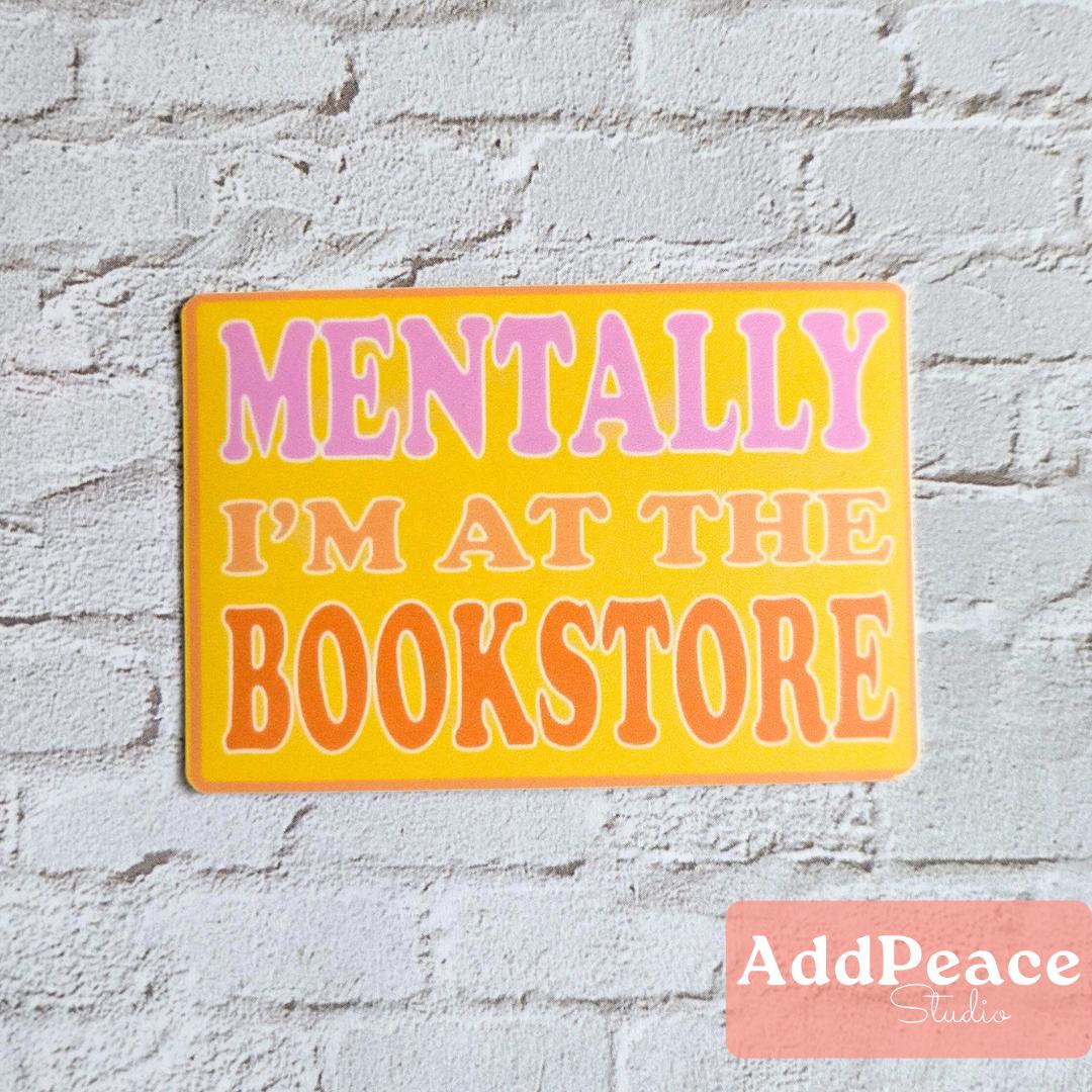 Sticker with 'Mentally I'm at the Bookstore' text on a white brick wall, featuring the brand 'AddPeace Studio'.