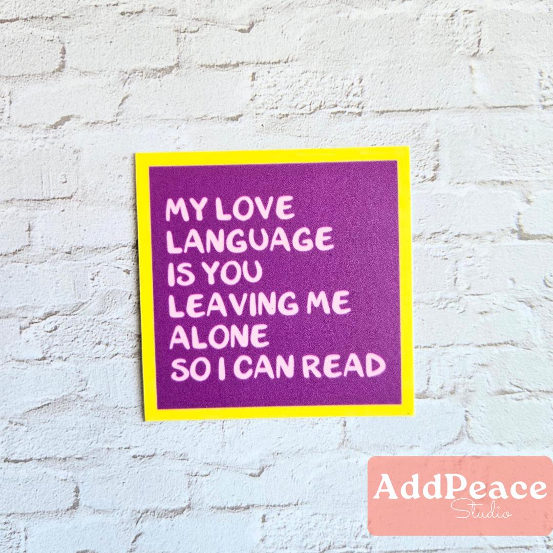Purple sticker with white text My love language is you leaving me alone so I can read on a white brick wall, featuring the brand 'AddPeace Studios'.