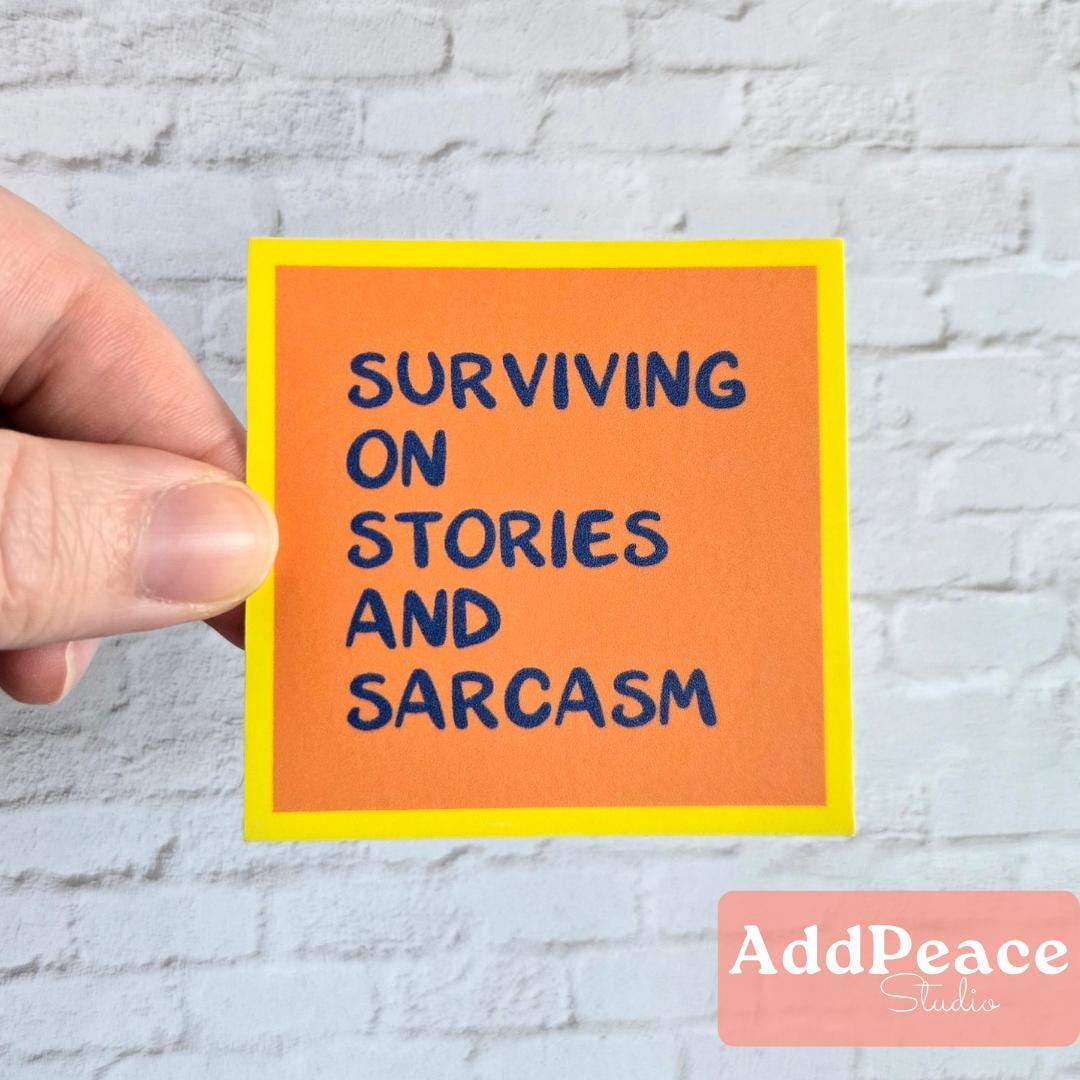 Hand holding an orange sticker with text 'Surviving on Stories and Sarcasm' against a light brick wall.