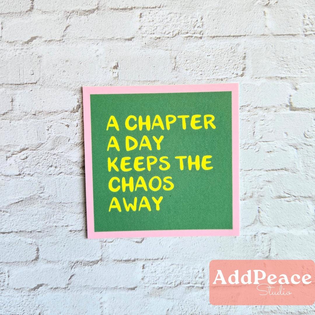 Green sticker with yellow text A Chapter a Day keeps the Chaos Away on a white brick wall, featuring the brand 'AddPeace'.