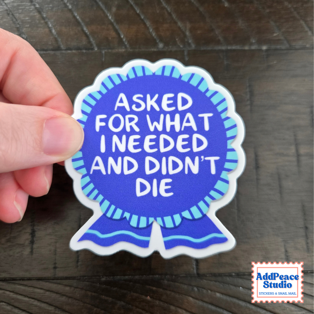 A hand holds a die-cut sticker shaped like a blue ribbon award. The sticker has white text reading 'ASKED FOR WHAT I NEEDED AND DIDN'T DIE' on a blue background with light blue stripes.