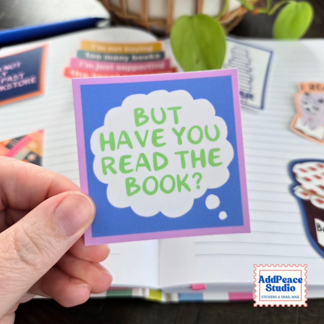 A hand holds a sticker with text But have you read the book in a white thought bubble with a blue and purple background.
