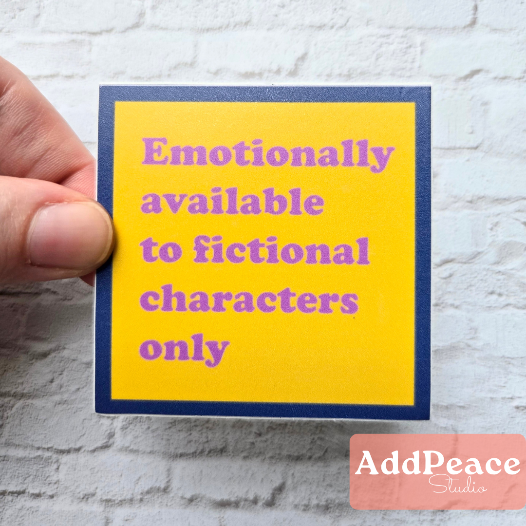 Hand holding a yellow card with text 'Emotionally available to fictional characters only' against a textured white background.