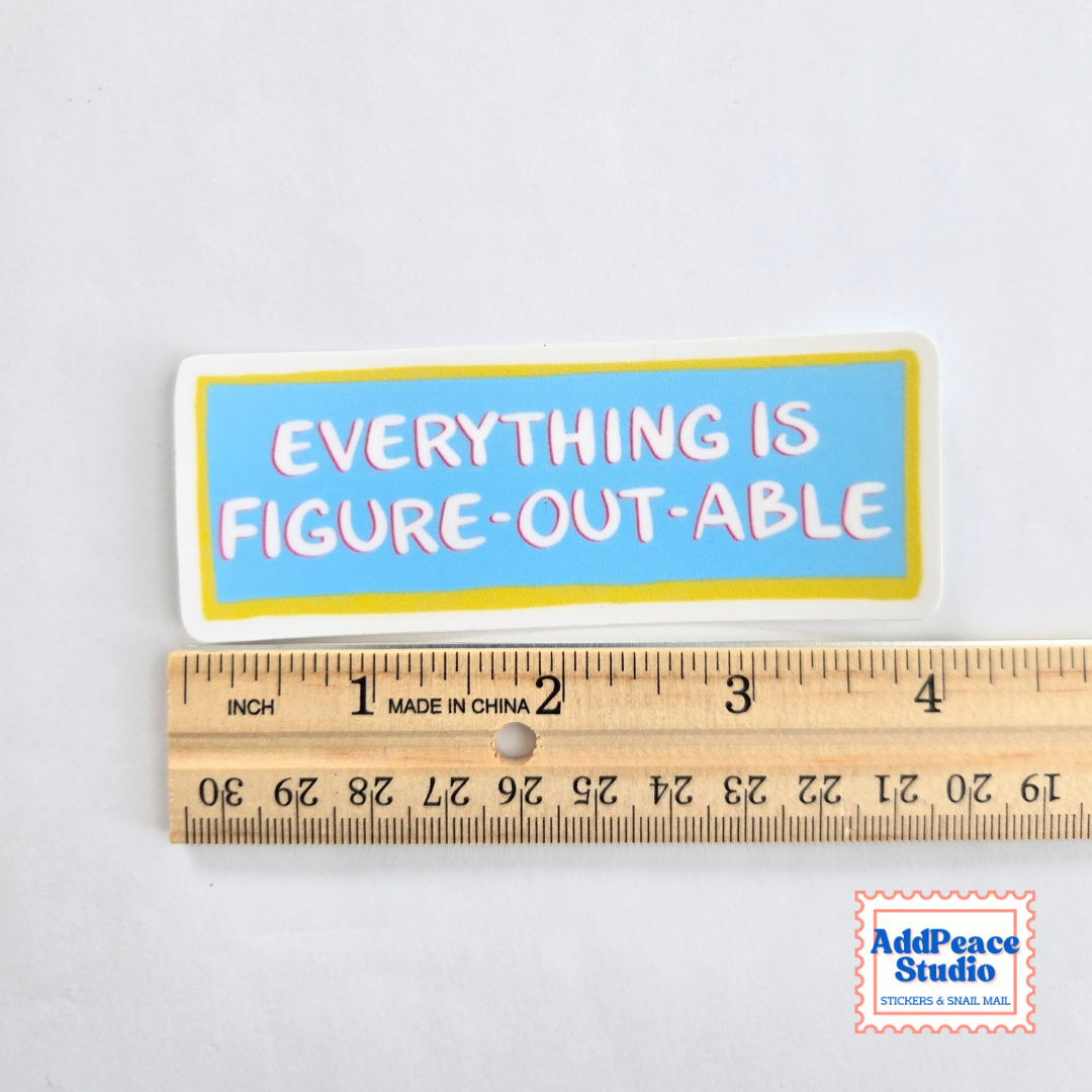 A rectangular sticker with the phrase 'EVERYTHING IS FIGURE-OUT-ABLE' in pink letters on a light blue background with a yellow border, shown above a wooden ruler for scale on a white background.