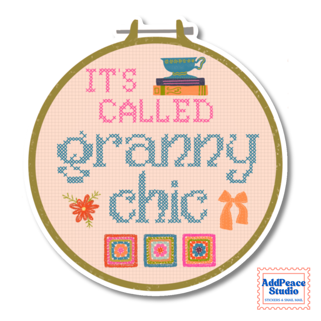 A circular embroidery hoop sticker containing a cross-stitch style design that reads “IT’S CALLED granny chic” in pink and blue thread, with small decorative motifs including books, a teacup, flowers, bows, and quilt squares. The hoop is shown on a white background with an AddPeace Studio logo in the lower right corner.