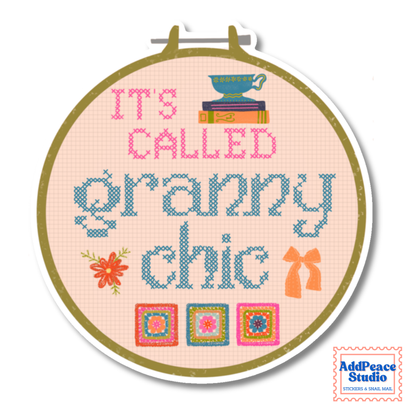 A circular embroidery hoop sticker containing a cross-stitch style design that reads “IT’S CALLED granny chic” in pink and blue thread, with small decorative motifs including books, a teacup, flowers, bows, and quilt squares. The hoop is shown on a white background with an AddPeace Studio logo in the lower right corner.