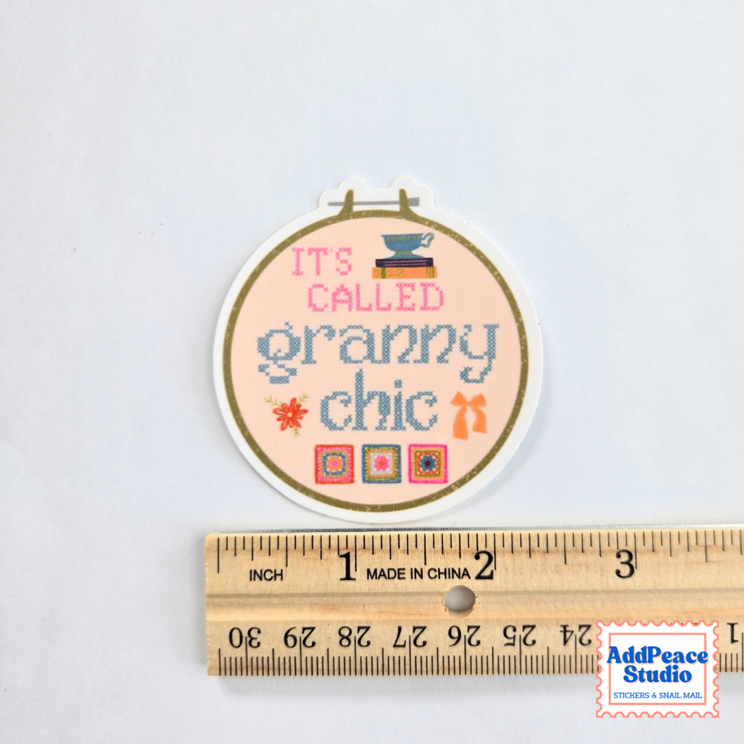 A circular sticker reading “ITS CALLED granny chic” with small decorative motifs, shown above a wooden ruler for scale on a white background. A small AddPeaceStudio watermark appears in the bottom right corner.