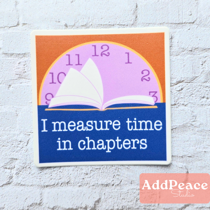 Decorative sticker with an open book and clock design, featuring the text 'I measure time in chapters' on a white brick background.