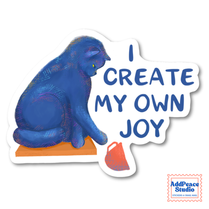 A die-cut sticker featuring a blue cat sitting on an orange pedestal next to the text 'I CREATE MY OWN JOY' in blue lettering on a white background. A small 'AddPeace Studio' brand mark is visible in the bottom right corner of the image.