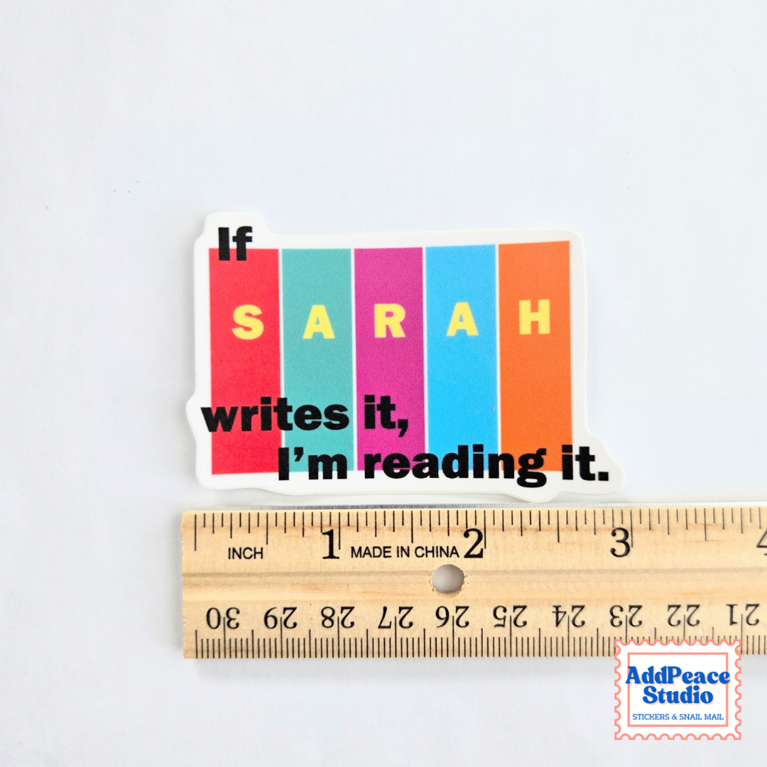 A die-cut sticker with the text 'If SARAH writes it, I'm reading it.' in black over six vertical color blocks (red, teal, magenta, blue, orange, and white), shown above a wooden ruler for scale on a white background.
