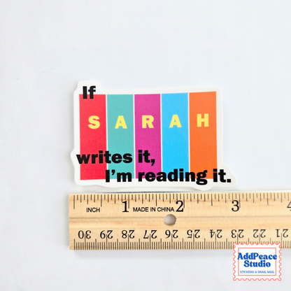 A die-cut sticker with the text 'If SARAH writes it, I'm reading it.' in black over six vertical color blocks (red, teal, magenta, blue, orange, and white), shown above a wooden ruler for scale on a white background.