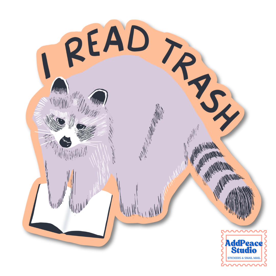 A die-cut sticker featuring a stylized raccoon reading an open book, with the text “I READ TRASH” arched above it. The sticker has a peach outline and is shown on a plain white background.