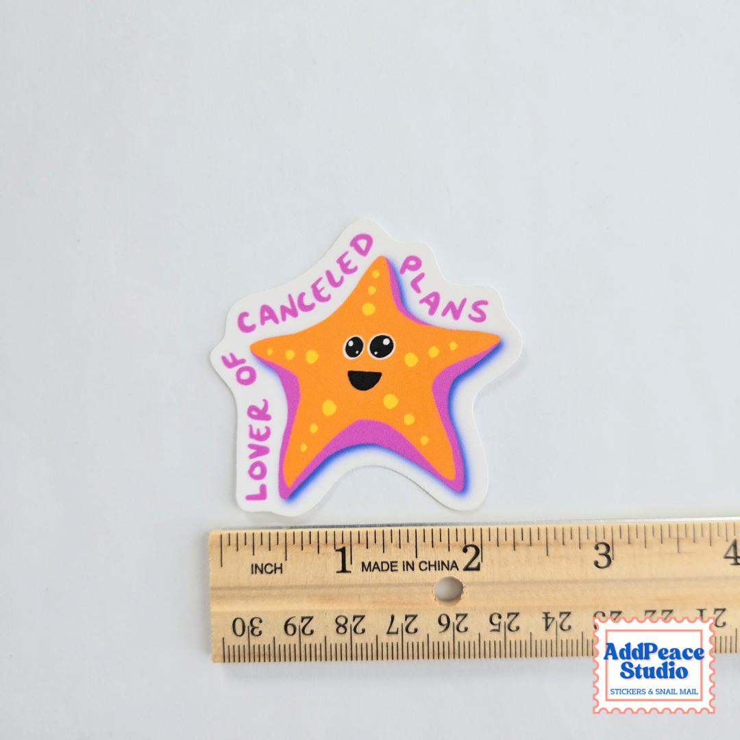 A die-cut sticker featuring a smiling orange starfish with the text 'LOVER OF CANCELED PLANS' in pink. The sticker is displayed above a wooden ruler on a plain white background, with an 'AddPeace Studio' watermark in the bottom right corner.
