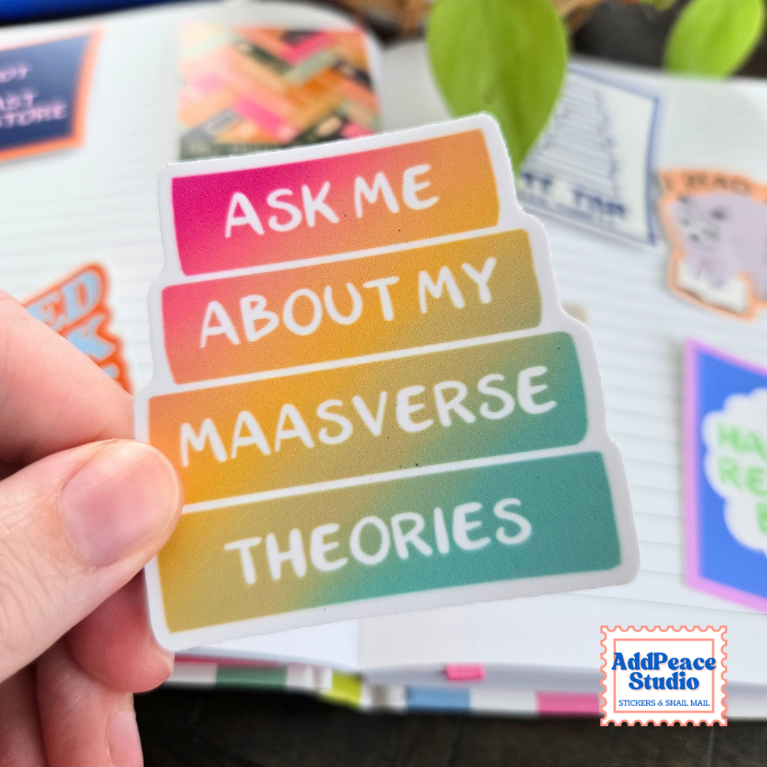 Close up of vinyl sticker in a rainbow color gradient book stack that says Ask me about my Maasverse theories, with AddPeace Studio stickers on an open notebook in the background.