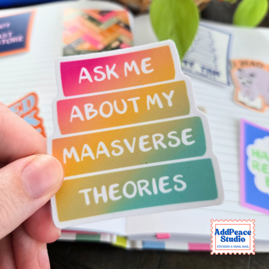 Close up of vinyl sticker in a rainbow color gradient book stack that says Ask me about my Maasverse theories, with AddPeace Studio stickers on an open notebook in the background.