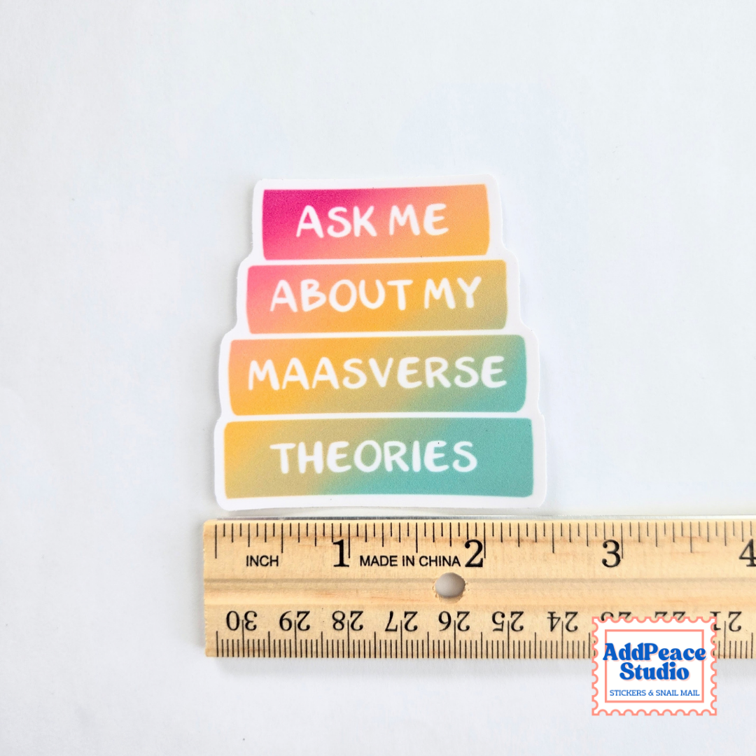 A colorful die-cut sticker with the text 'ASK ME ABOUT MY MAASVERSE THEORIES' in white lettering on four horizontal book spines, shown above a wooden ruler for scale on a white background.