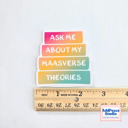 A colorful die-cut sticker with the text 'ASK ME ABOUT MY MAASVERSE THEORIES' in white lettering on four horizontal book spines, shown above a wooden ruler for scale on a white background.