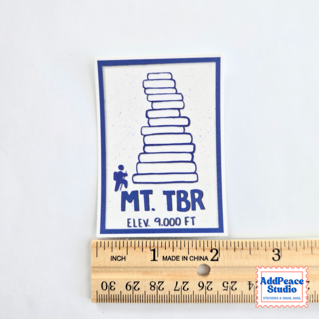 A rectangular white sticker with a blue border and graphic of a book stack, labeled 'MT. TBR' and 'ELEV. 9000 FT