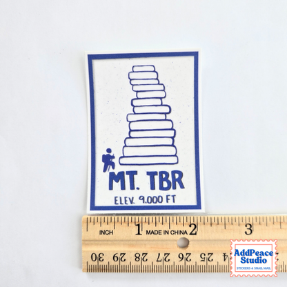 A rectangular white sticker with a blue border and graphic of a book stack, labeled 'MT. TBR' and 'ELEV. 9000 FT