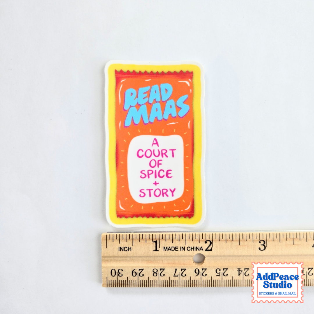 A rectangular sticker featuring a stylized orange and taco sauce packet design with the text 'READ MAAS' in blue and 'A COURT OF SPICE + STORY' in pink, shown above a wooden ruler for scale on a white background.