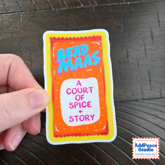 A hand holds a die-cut sticker shaped like a colorful sauce packet. The sticker reads “READ MAAS” in blue letters and “A COURT OF SPICE + STORY” in pink on a white panel, with orange, yellow, and blue colors.