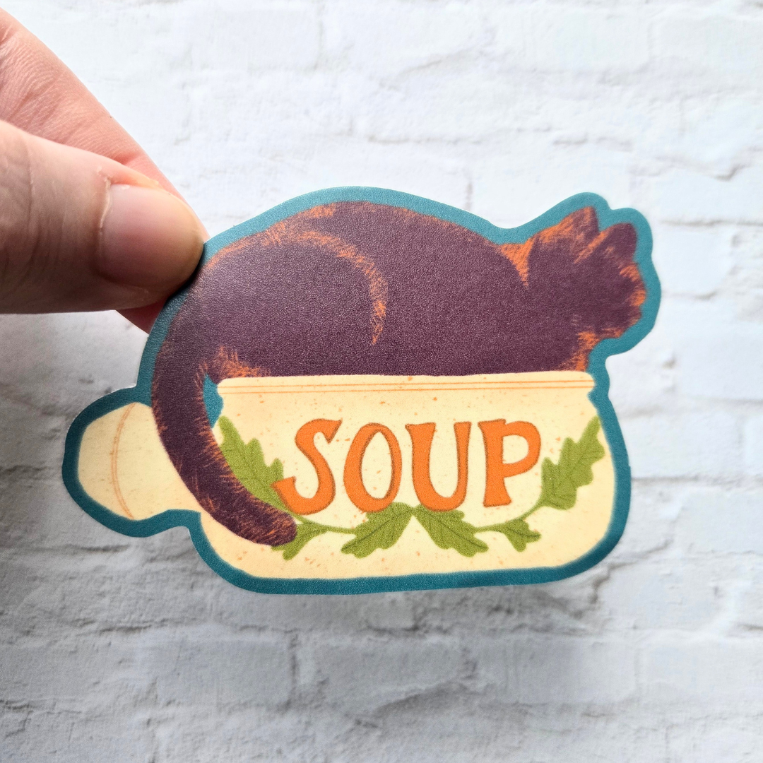Sticker of a soup bowl with 'SOUP' text held by a hand on a light background