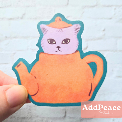 Sticker of a cat inside a teapot held by a hand on a light blue brick background with 'AddPeace Studio' branding.