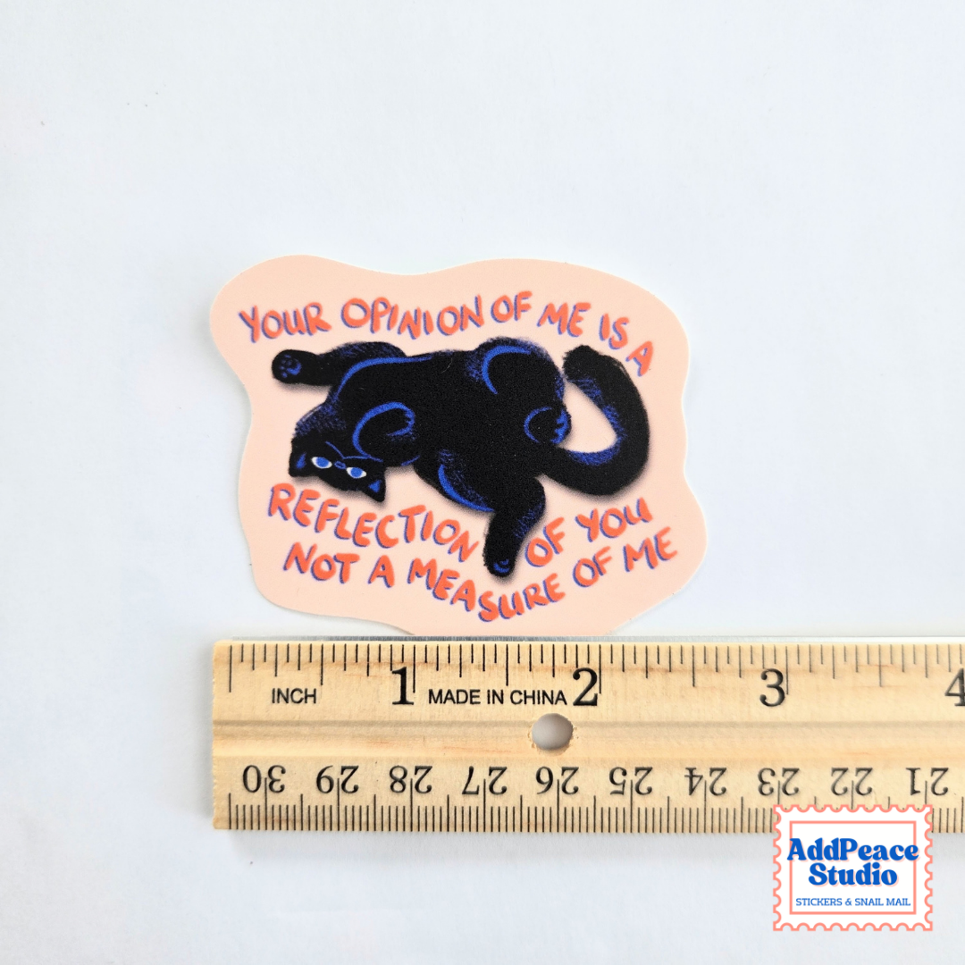 A die-cut sticker featuring a black cat silhouette with blue accents and the text 'YOUR OPINION OF ME IS A REFLECTION OF YOU NOT A MEASURE OF ME' in orange-red lettering on a pale peach background. The sticker is shown above a wooden ruler for scale, with an 'AddPeace Studio' watermark in the bottom right corner.