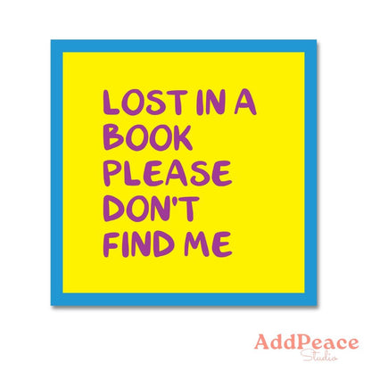 Yellow sticker with purple text 'Lost in a book please don't find me' on a white background, framed in blue.