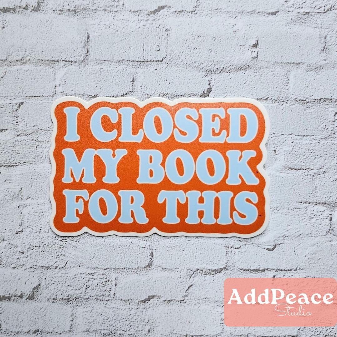 Sticker with 'I Closed My Book For This' text on a white brick wall, featuring the AddPeace Studios logo.