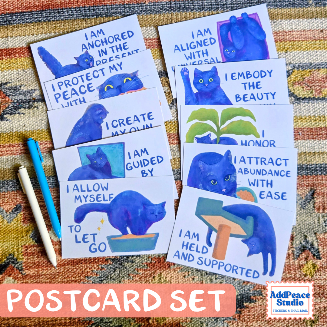 A set of printed postcards featuring blue cat illustrations and affirmational phrases, arranged on a patterned fabric background with two colored pencils. A pink banner at the bottom reads 'POSTCARD SET' and the AddPeaceStudio logo appears in the lower right corner.