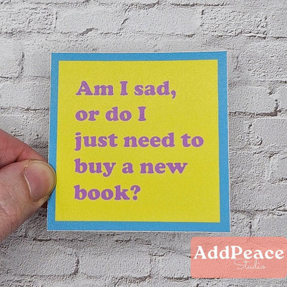 Hand holding a yellow sticker with purple text against a gray textured wall, featuring 'AddPeace Studios' logo.
