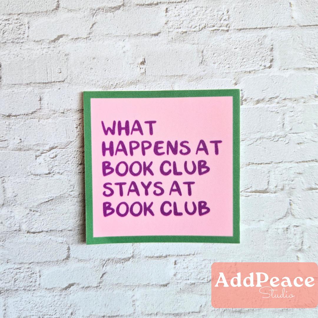 Pink sticker with text 'What happens at book club stays at book club' on a white brick wall, featuring AddPeace Studios branding.