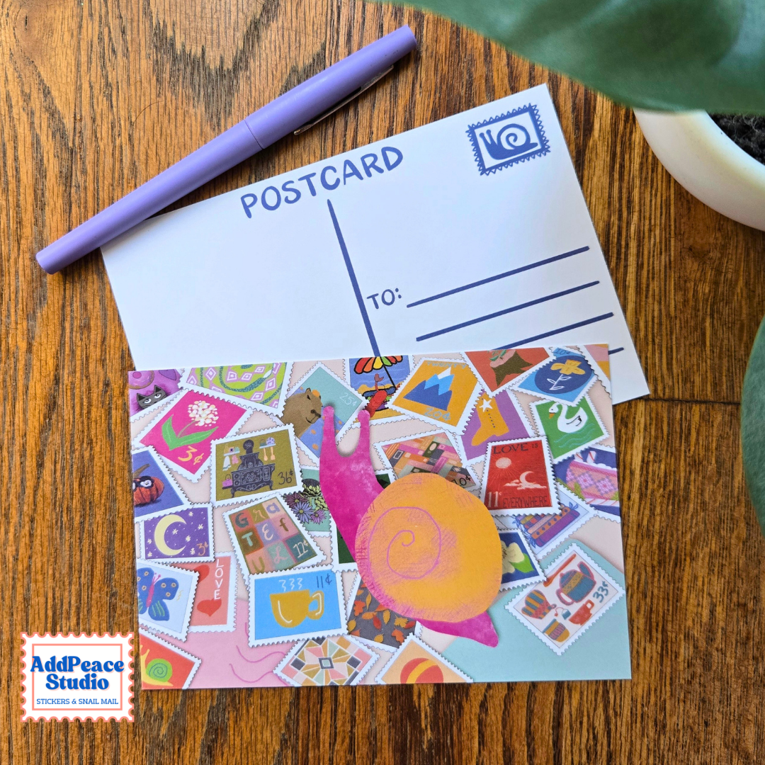 A colorful postcard featuring a pink snail and yellow-orange shell on a background of illustrated postage stamps, displayed on a wooden table next to a purple pen and a postcard template. The AddPeace Studio logo is visible in the bottom-left corner.