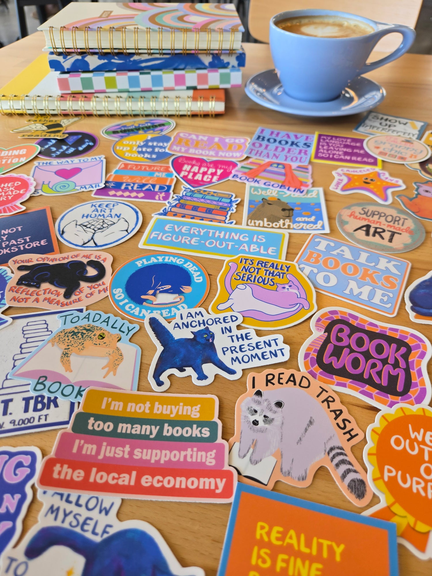 Table covered with colorful stickers with a latte and stack of notebooks in the background